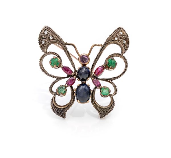 Spilla antica a farfalla in oro, argento diamanti, zaffiri in taglio cabochon, rubini in taglio navette e tondo, smeraldi in taglio rotondo
