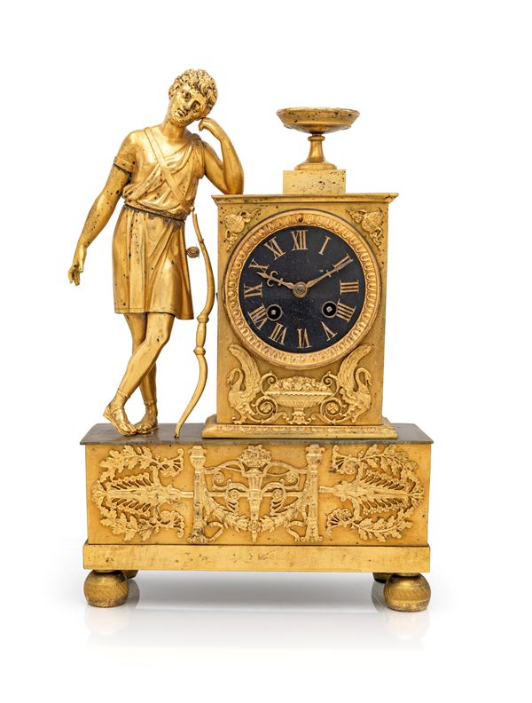Orologio da camino in bronzo dorato con figura di Amore con arco e quadrante nero a numero romani firmato 