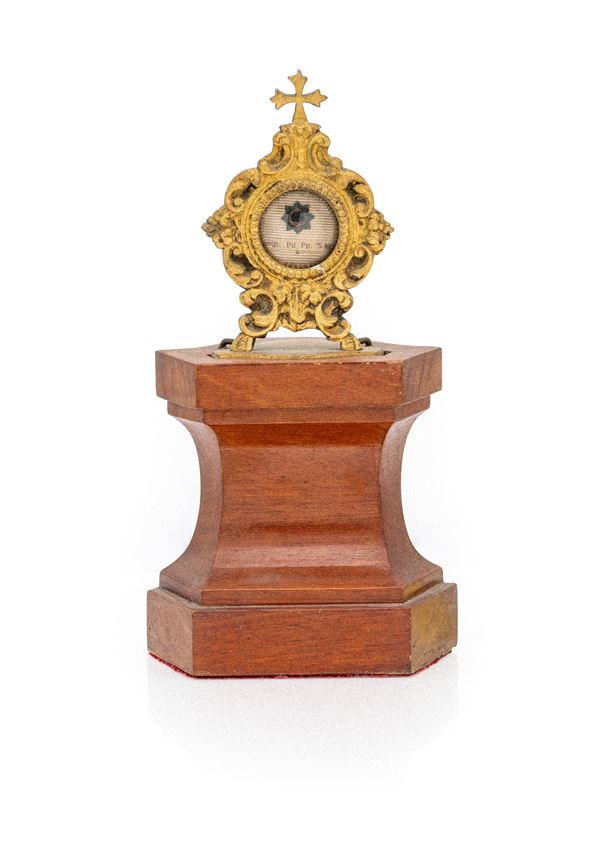 Piccolo reliquiario in ottone dorato su piedistallo in legno